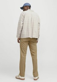 Plaid button-up shirt in light beige and pastel hues, paired with tan chinos and a blue cap. Casual footwear with white and brown accents.