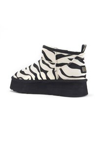 Ankle čizmica sa zebrastim uzorkom u crno-bijeloj boji, sa ravnim crnim đonom i suptilnim brendiranjem na peti. Izrađene od mekog, teksturiranog materijala.