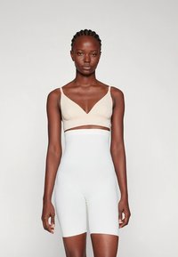 Beige, seamless bralette with a V-neck and wide straps, paired with high-waisted, tight-fitting white shorts made of smooth fabric.