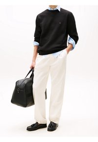 Felpa nera con collo tondo, camicia a righe blu chiaro sotto, pantaloni bianchi e borsa in pelle nera. Mocassini casual completano il look.