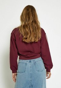 Burgundy sweatshirt with long sleeves and ribbed hem, paired with a light blue denim skirt featuring two back pockets.