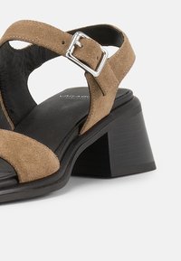 Καφέ σανδάλι από σουέντ με ανοιχτό δάχτυλο, ρυθμιζόμενο λουράκι με ασημένια αγκράφα και χοντρό μαύρο τακούνι block.