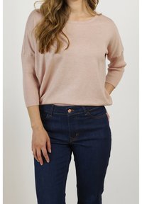 Ljust rosa stickad tröja med rund halsringning, ribbade ärmslut, kombinerad med mörkblå denimjeans med knappstängning och sömnadsdetaljer.