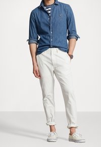 Jeansskjorta med knappar, vita chinos och krämfärgade sneakers. Funktioner inkluderar uppvikta ärmar, randig innertröja och armbandsur.