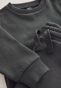 Tamnosivi pamučni duks s rebrastim ovratnikom i manžetama, upareni s odgovarajućim joggericama koje imaju prikupljeni elastični pojas i vezice.