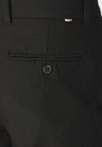 Los pantalones negros cuentan con un bolsillo trasero con cierre de botón, diseño ajustado, textura suave y un borde delgado a lo largo del borde del bolsillo.