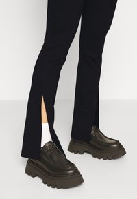 Zwarte broeken met zijsplitten, gecombineerd met grove zwarte leren schoenen met dikke zolen en contrasterende witte sokken.