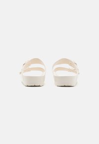 Lys beige sandaler med to justerbare stropper, teksturert fotseng og en tykk såle med et sikksakkmønster for grep.