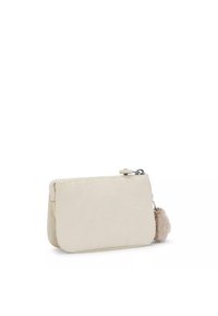 Borsetta color crema realizzata in materiale morbido, dotata di chiusura con zip e un morbido pom-pom marrone chiaro attaccato di lato.