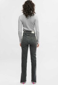 Hoge taille, donkergrijze jeans met subtiele textuur, een rafelige zoom en contrasterende stiksels, gecombineerd met een aansluitende lichtgrijze geribde trui.