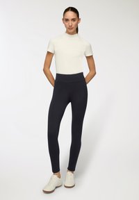 Biały top z krótkim rękawem w połączeniu z czarnymi legginsami o wysokim stanie. Legginsy mają gładką teksturę i długość do kostek, dopełnione białymi butami.