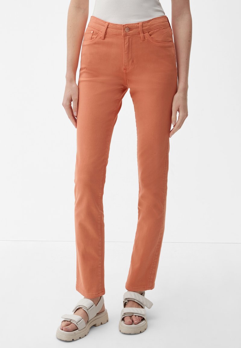 Pomarańczowe dżinsy bawełniane o slim fit, z zapięciem na guzik, szlufkami na pasek i kieszeniami z przodu. W połączeniu z beżowymi sandałami.