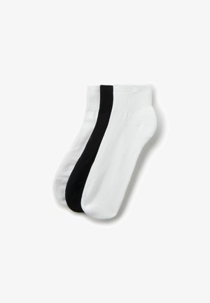 Trois chaussettes basses, deux blanches et une noire, empilées côte à côte sur un fond blanc.