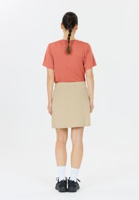 Kurzärmliges, korallenfarbenes Hemd und beiges Skort, mit glatter Textur, einfachem Design und einer Gesäßtasche am Skort. Schwarze Schuhe und weiße Socken.