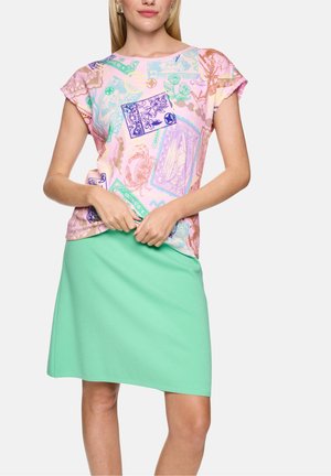 Femme portant un haut rose pastel à motifs bleus et verts et une jupe unie vert clair, longueur genoux.