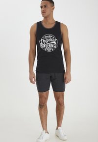 Top senza maniche nero con grafica bianca "Original Raw Denim Co.", abbinato a pantaloni corti grigio scuro e sneakers bianche.