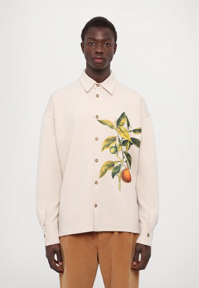 Gaišs bežs krekls ar botānisku rakstu, kas veidots ar dzeltenām lapām un augļiem, pogājams priekšpuse un ar piedurknēm, kas ir uzkāpušas. Gluda tekstūra.