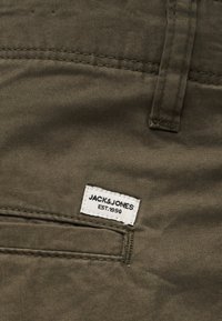 Κοντινή λήψη καφέ υφασμάτινου παντελονιού που δείχνει μια πίσω τσέπη με μια λευκή ετικέτα της μάρκας Jack & Jones ραμμένη από πάνω.