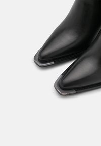 Czarne skórzane botki sięgające kostki z ostrym noskiem, z metalicznym akcentem na końcu oraz elegancką, gładką fakturą.