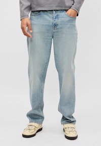 Ανοιχτό μπλε τζιν παντελόνι με άνετη εφαρμογή, που διαθέτει κλασικό σχέδιο πέντε τσεπών και διακριτική φθορά. Συνδυασμένο με κρέμ αθλητικά παπούτσια.