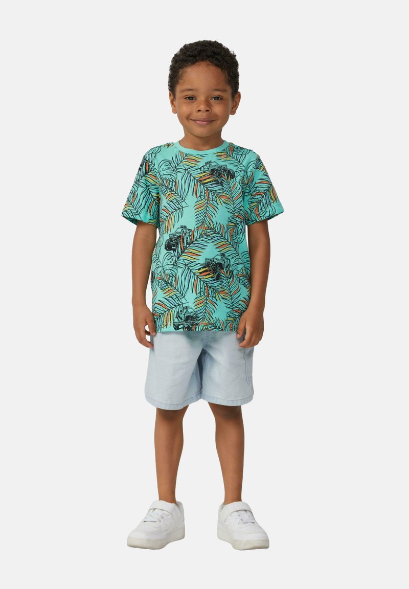 Turquoise t-shirt met korte mouwen met een zwart tropisch bladenpatroon, gecombineerd met lichtblauwe shorts en witte sneakers.