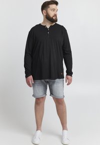 Fekete, hosszú ujjú henley póló, három kis gombbal, világosszürke farmerkorttával párosítva. Lazán illeszkedő fazon, felgöngyölt ujjak.