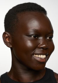Porträtt av en person med mörk hy, kort texturerat hår och ett svagt leende. Klädd i en svart ärmlös topp, hyn har ett slätt och friskt utseende.