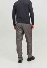 Grauer Pullover mit langen Ärmeln, kombiniert mit grauen, gestreiften Hosen. Das Outfit zeichnet sich durch einen strukturierten Stoff und einen lässigen Schnitt aus.