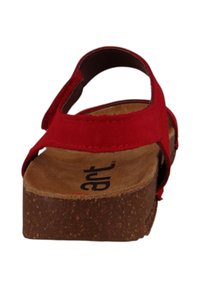 Sandalia roja con suela de corcho, correas ajustables y plantilla suave. Presenta una textura lisa y un diseño informal adecuado para el clima cálido.