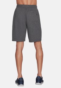 Pantalones cortos deportivos grises con una cinturilla elástica, tela texturizada y un bolsillo trasero. Usados con zapatos azul marino sobre un fondo liso.