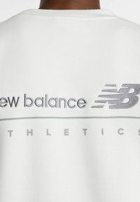 Felpa bianca con collo rotondo. Presenta testo ricamato grigio "new balance" e "ATHLETICS", con accenti a linee orizzontali.