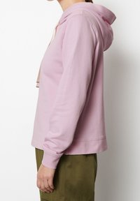 Sudadera con capucha rosa hecha de una suave mezcla de algodón, que presenta un corte relajado, puños acanalados y detalles laterales. Combinada con pantalones verde oliva.