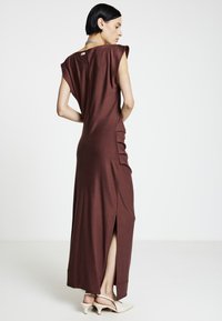 Robe maxi marron à coupe décontractée, manches courtes raglan, fentes latérales et tissu texturé. Caractéristiques : petite ouverture dans le dos et design minimaliste.