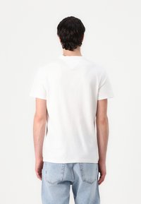 Weißes Baumwoll-T-Shirt mit kurzen Ärmeln, Rundhalsausschnitt und geradem Schnitt. Kombiniert mit hellblauen Jeans. Einfaches, unauffälliges Design.
