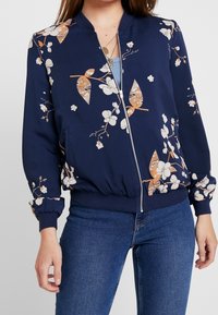 Námořnická bomber bunda s květinovým potiskem, se zipem vpředu, žebrovanými manžetami a pasem, vyrobená z hladké tkaniny s lehkou strukturou.