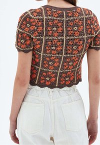 Top de crochet recortado con cuadrados florales en tonos naranja y beige, combinado con pantalones blancos de tiro alto, visto desde la espalda.
