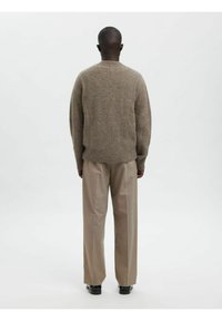 Brūns adīts džemperis ar apaļu kaklu, ar vaļēju piegriezumu un ribotu apakšmalu. Saskaņots ar gaiši bēšām pielāgotām biksēm un melniem apaviem.