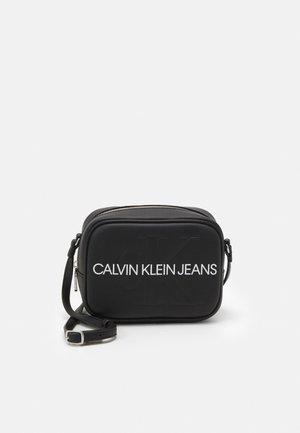 Černá crossbody taška Calvin Klein Jeans s bílým logem a nastavitelným popruhem na bílém pozadí.