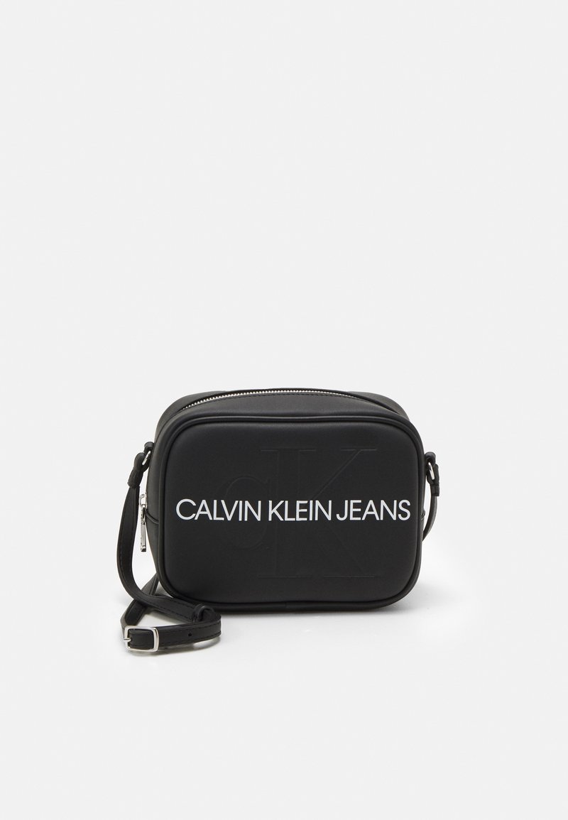 Černá crossbody taška Calvin Klein Jeans s bílým logem a nastavitelným popruhem na bílém pozadí.