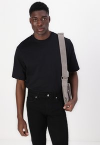 T-shirt noir à manches courtes associé à un jean noir et un sac bandoulière gris. Les caractéristiques comprennent une coupe décontractée et un design minimaliste.