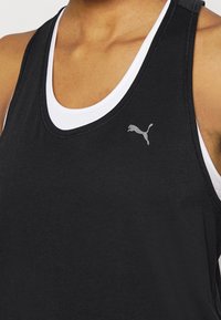 Débardeur noir sans manches avec un col rond, superposé à un débardeur blanc. Présente un logo Puma gris sur la partie gauche de la poitrine.