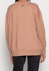 Felpa oversize in tessuto rosa chiaro, con polsini e orlo a costine, dotata di un piccolo logo marrone sul retro vicino al collo.