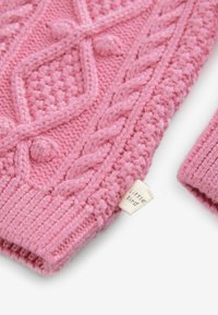 Ružový pletený sveter s textúrovanými káblami a guličkami; obsahuje malú nášivku s nápisom "malý vták" na lemovaní.