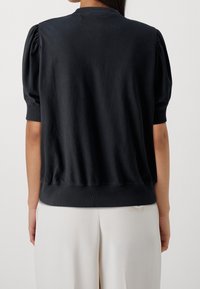Suéter negro con mangas cortas abullonadas y puños acanalados. Presenta un corte holgado y cintura fruncida. Material de algodón suave y ligero.