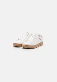 Białe sneakersy wykonane ze skóry z początkową teksturowaną białą cholewką, brązową gumową podeszwą i czerwonym akcentem. Płaskie sznurowadła i perforowane boczne panele.