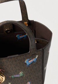 Καφέ τσάντα ώμου Michael Kors με πολύχρωμες εικονογραφήσεις αλόγων και χρυσά εξαρτήματα, εμφανίζοντας λαβές στην κορυφή και εσωτερικό κλείσιμο με κουμπί.