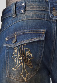 Jeans dżinsowe w ciemnoniebieskim odcieniu, z złotymi przeszyciami i haftowanym wzorem na tylnej kieszeni, z metalowymi akcentami.
