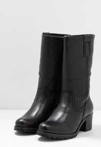 Botas de cuero negras hasta el tobillo con un acabado texturizado, puntera redonda y tacón cuadrado. Presentan detalles cosidos y una suela lisa.