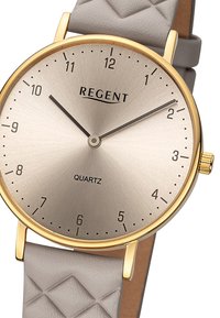 Montre à quartz avec un cadran argenté brossé, une lunette dorée et un bracelet en cuir matelassé gris ; dispose de repères d'heures simples et d'aiguilles.