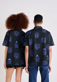 Zwarte t-shirt met korte mouwen, voorzien van blauwe grafische patronen, waaronder gezichten en tekst. Casual ontwerp met een losse pasvorm, geschikt voor unisex gebruik.